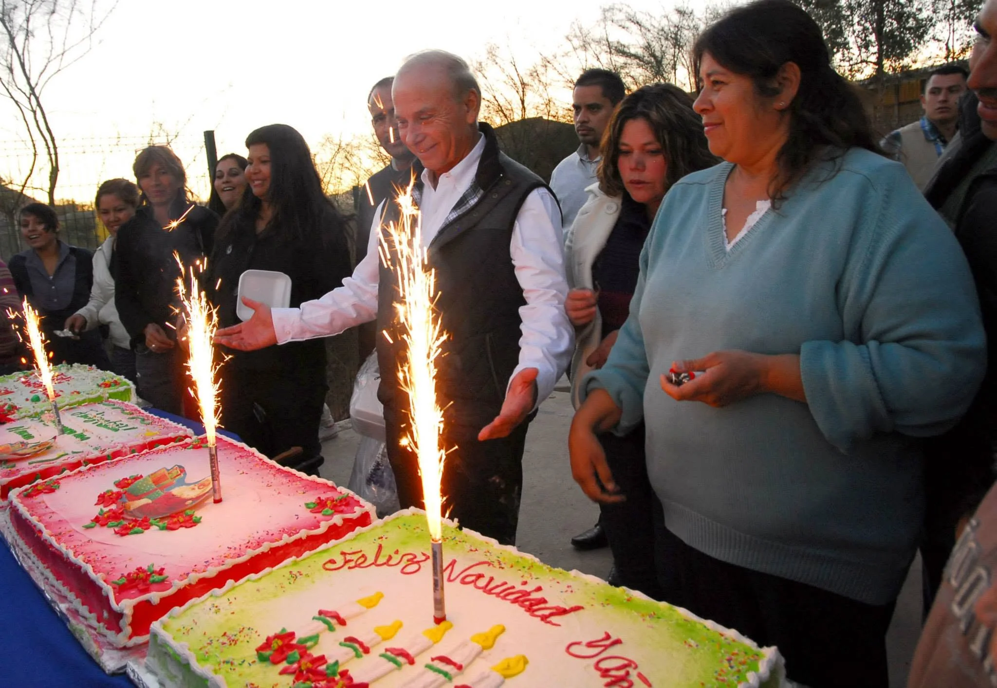 Javier Gándara Magaña posando de tras de dos pasteles mientras sonríe con la gente
